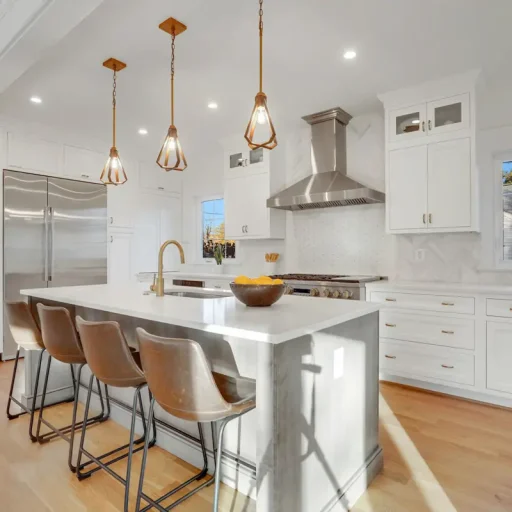 Modern kitchen with island, chairs, and hanging lights.